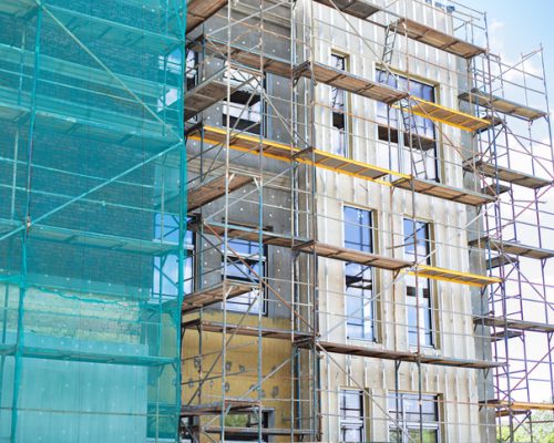 Building under construction against blue sky. New high-rise building under construction with brick work and wooden scaffolding. Concrete building under construction.